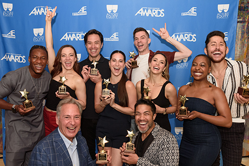 Ten members of the chorus of 'The Heart of Rock and Roll' holding their awards in front of a step-and-repeat for the Actors' Equity Foundation Awards.