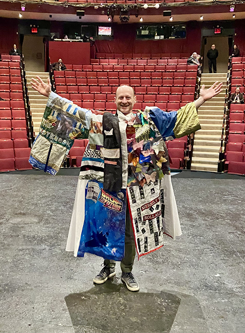 Jeremy Davis stands onstage in the Robe with his back to the house, smiling in the Robe with his arms reached up.