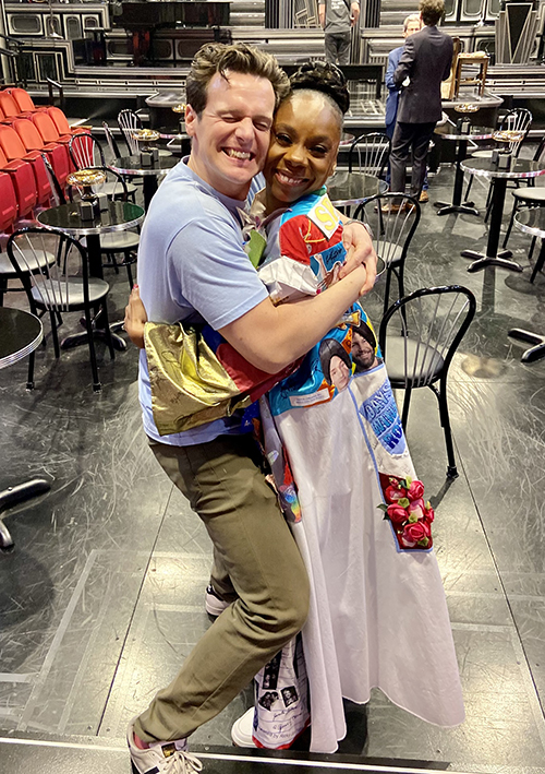 Petinaud in the Robe and Jonathan Grodd hug and smile together in front of the theater's house seating that includes cafe tabels and chairs.